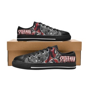 May include: Black canvas sneakers featuring a Spider-Man design. The shoes have a black toe cap, white laces, and a black sole with a white stripe. The Spider-Man logo is prominently displayed on the side.