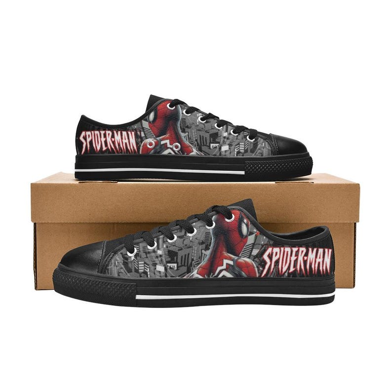 May include: Black canvas sneakers featuring a Spider-Man design. The shoes have a black toe cap, white laces, and a black sole with a white stripe. The Spider-Man logo is prominently displayed on the side.