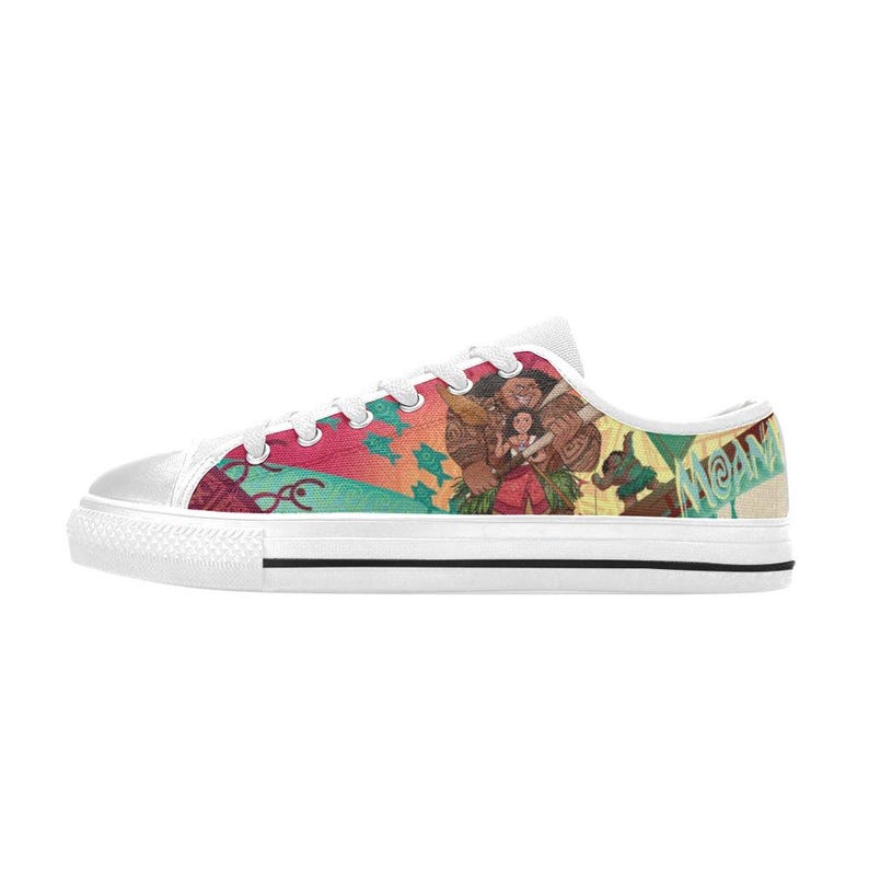 May include: White canvas sneakers with a colorful graphic featuring characters from the animated film "Moana." The design includes images of the characters, fish, and the word "Moana" in green. The shoes have white laces and a white rubber sole.
