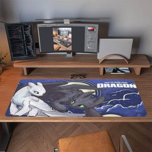 Può includere: Tappetino per scrivania rettangolare con personaggi di "Dragon Trainer". Il design include un drago bianco a sinistra e un drago nero a destra, su uno sfondo di cielo blu con nuvole bianche. Il testo "HOW TO TRAIN YOUR DRAGON" è visualizzato.