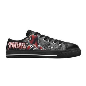 May include: Black low-top canvas sneakers featuring a Spider-Man design. The sneakers have a black rubber sole and laces. The Spider-Man graphic is in red and black, with the words "SPIDER-MAN" in red on the side.