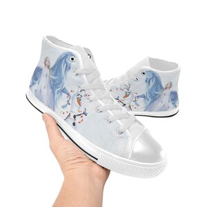 Pu&ograve; includere: Sneakers alte in tela bianca con una stampa raffigurante un personaggio biondo in un lungo abito bianco, un cavallo blu e un pupazzo di neve. Le scarpe presentano lacci bianchi, punte in gomma bianca e un sottile bordo nero sulla suola.