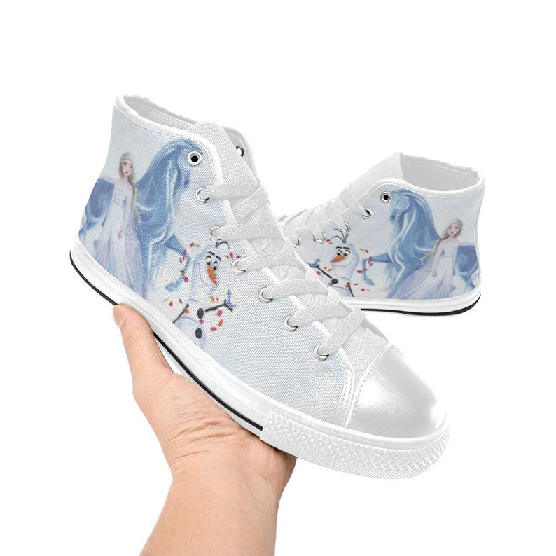 Pu&ograve; includere: Sneakers alte in tela bianca con una stampa raffigurante un personaggio biondo in un lungo abito bianco, un cavallo blu e un pupazzo di neve. Le scarpe presentano lacci bianchi, punte in gomma bianca e un sottile bordo nero sulla suola.