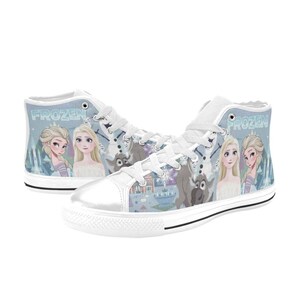 Pode incluir: Um par de t&eacute;nis de cano alto em lona branca com uma impress&atilde;o gr&aacute;fica azul-clara de personagens do filme Frozen, incluindo Elsa, Anna, Olaf e Sven. Os sapatos t&ecirc;m atacadores brancos, biqueiras de borracha branca e a palavra Frozen.