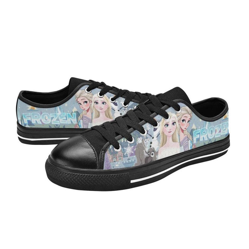May include: Low-top sneakers with black laces, black toe caps, and black soles. The side panels feature a light blue graphic print of characters from Frozen, including Elsa and Anna, with the word Frozen printed in a stylized blue font.