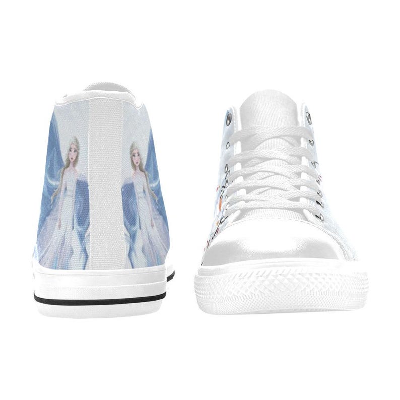 Pu&ograve; includere: Un paio di scarpe da ginnastica alte in tela bianca con una stampa grafica di un personaggio biondo in un lungo abito bianco e blu. Le scarpe hanno lacci bianchi, punte in gomma bianca e una sottile striscia nera lungo la base delle suole.
