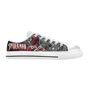 May include: White canvas sneakers featuring a Spider-Man design. The side of the shoe displays the Spider-Man logo in red and black, with an image of Spider-Man. The background has a cityscape design.
