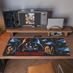 Könnte beinhalten: Schwarzes Mauspad mit Darth Vader-Motiv. Das Design zeigt Darth Vaders Helm, den Schriftzug "Darth Vader" in Rot und blaue Raumschiffe vor einem Sternenhintergrund. Für den Computertisch.