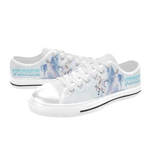 Peut inclure: Baskets basses en toile blanche avec un motif imprim&eacute; repr&eacute;sentant Elsa et Olaf de Frozen. Les chaussures ont des lacets blancs, un bout en caoutchouc blanc et une bande noire le long de la semelle. Le mot Frozen est imprim&eacute; en bleu sur le c&ocirc;t&eacute;.
