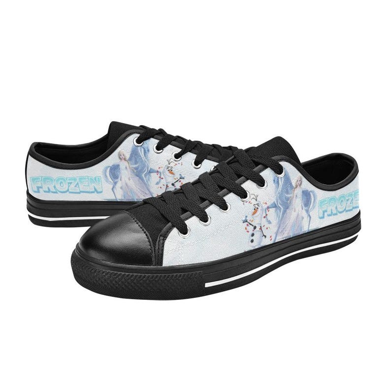 Peut inclure: Baskets basses en toile avec une base blanche et un imprim&eacute; graphique Frozen repr&eacute;sentant Elsa et Olaf. Les chaussures ont des lacets noirs, un bout noir et une semelle noire avec une bande blanche. Le mot Frozen est imprim&eacute; en bleu sur le c&ocirc;t&eacute;.