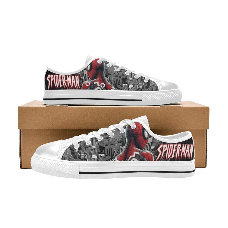 May include: White canvas sneakers featuring a Spiderman design. The shoes have a black and white cityscape pattern with a red and black Spiderman graphic on the side. The word "SPIDER-MAN" is printed in red.