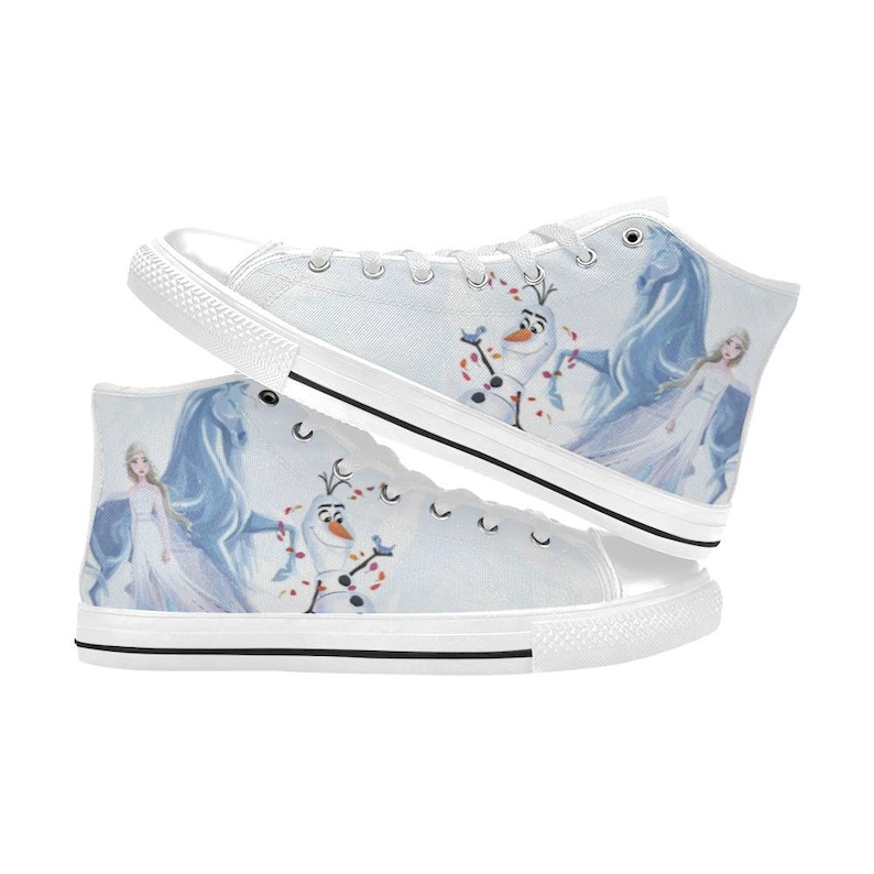 Pu&ograve; includere: Un paio di scarpe da ginnastica alte in tela bianca con una stampa di un personaggio biondo in abito bianco, un pupazzo di neve e un cavallo blu. Le scarpe hanno lacci bianchi, punte in gomma bianca e una striscia nera sulla suola.