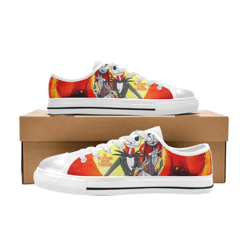May include: Low-top canvas trainers featuring a vibrant red and yellow graphic print of Jack Skellington and Sally from The Nightmare Before Christmas. The shoes have white laces, white rubber toe caps, and white soles with a thin black stripe.