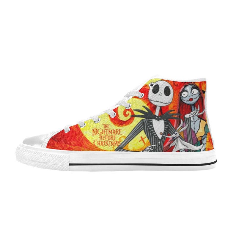 May include: A high-top canvas sneaker featuring a vibrant orange and yellow background with a graphic print of Jack Skellington, Sally, and Zero from The Nightmare Before Christmas. The shoe has white laces, a white rubber toe cap, and a white sole.