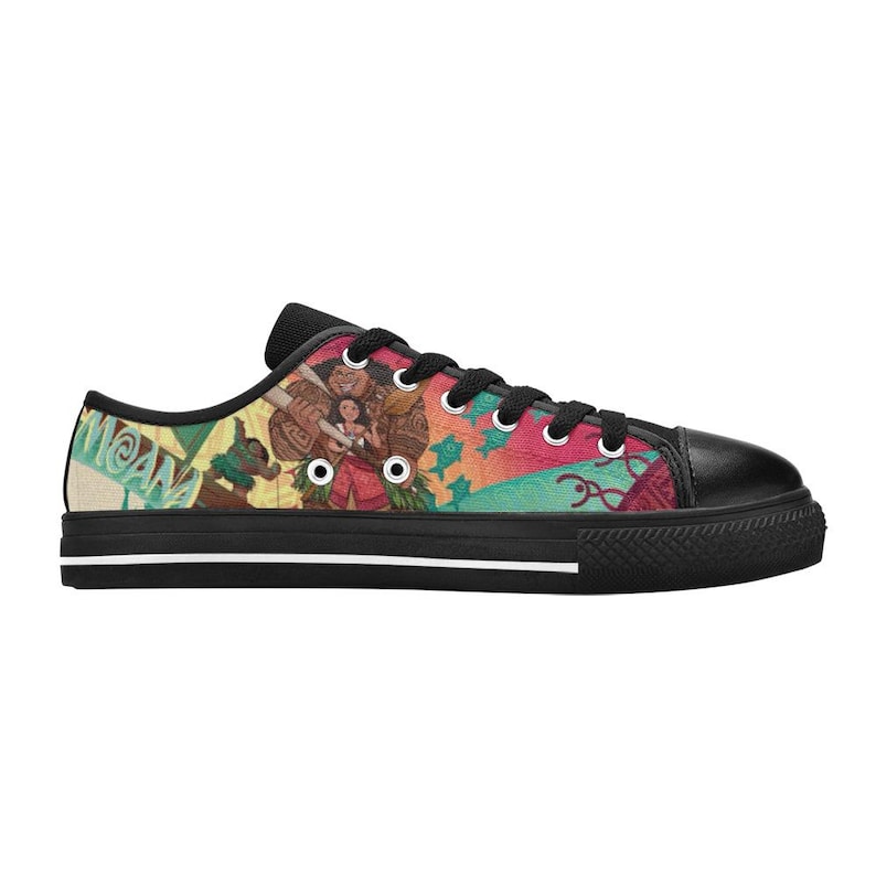 May include: Black canvas sneakers with a colorful graphic print featuring characters and the word "MOANA". The shoes have black laces, a black rubber toe cap, and a black rubber sole with a white stripe.