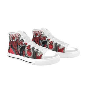 May include: A pair of white high-top sneakers featuring a comic book graphic print of the character Spider-Man in red and black. The shoes have white laces, white rubber toe caps, and white rubber soles with a thin black stripe along the edge.