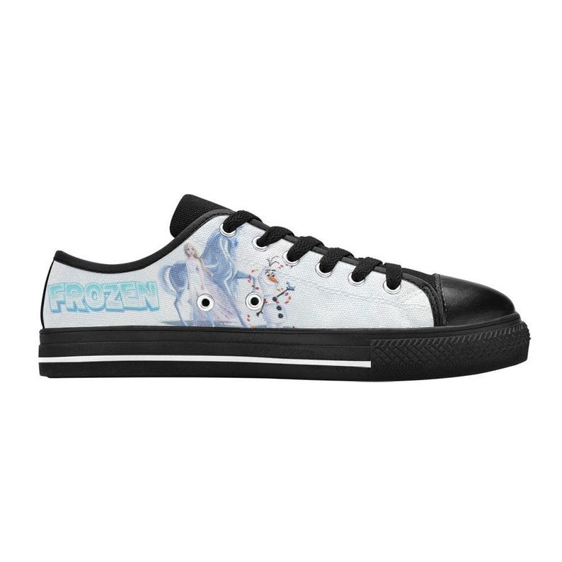 Peut inclure: Une basket basse en toile avec une base blanche et un motif imprim&eacute; repr&eacute;sentant Elsa et Olaf de Frozen. La chaussure poss&egrave;de des lacets noirs, un bout noir et une semelle en caoutchouc noire avec une fine ligne blanche sur le c&ocirc;t&eacute;.