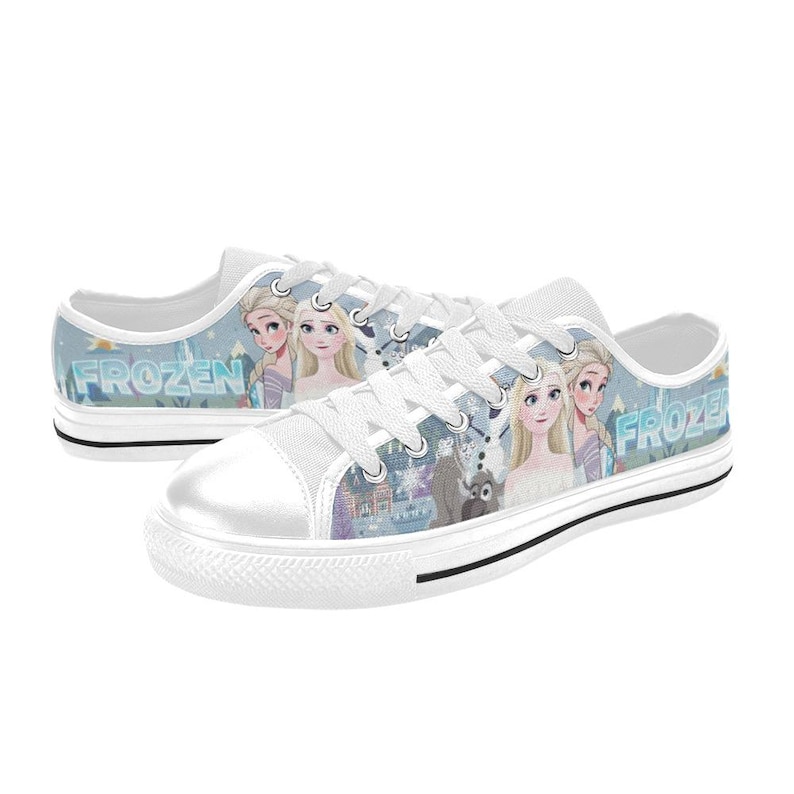 May include: Low-top canvas sneakers featuring a light blue and white Frozen theme with printed graphics of Elsa, Anna, and Olaf. The shoes have white laces, white rubber toe caps, and white soles with a black stripe detail along the side.