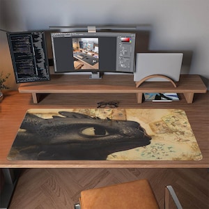 Può includere: Tappetino per mouse nero con un primo piano dell'occhio e della testa di un drago. Il design è ambientato su uno sfondo di mappa vintage. Il tappetino è rettangolare e si trova su una scrivania di legno, con monitor di computer e accessori visibili.