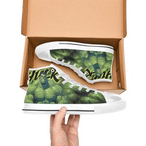 Puede incluir: Zapatillas de lona de caña alta con un gráfico del personaje Hulk en verde y la palabra HULK en letras negras. El calzado tiene cordones blancos, punteras de goma blanca y suelas de goma blanca, presentadas en una caja de cartón marrón.
