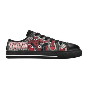 May include: A low-top sneaker featuring a black rubber sole with a white stripe and a black canvas upper printed with a comic book graphic of Spider-Man. The design includes the red and blue character in various poses and the text Spider-Man.