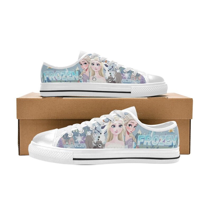 May include: Low-top canvas sneakers featuring a light blue and white Frozen theme print with characters Elsa, Anna, and Olaf. The shoes have white laces, white rubber toe caps, and white rubber soles with a black stripe detail along the base.