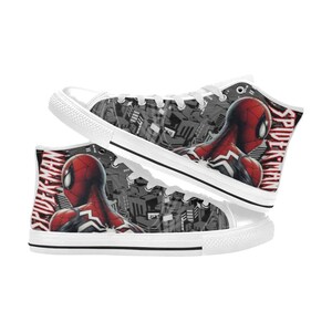 May include: White high-top sneakers featuring a Spider-Man design. The sneakers have a red and black Spider-Man graphic on the sides, with the word "Spider-Man" printed in red. The background is a gray and black cityscape.