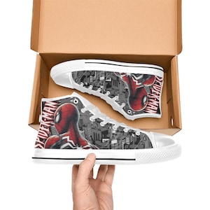May include: High-top canvas sneakers featuring a Spider-Man design. The shoes have a white rubber sole and laces, with a black and gray cityscape background. The Spider-Man graphic is red and black, with the word "SPIDER-MAN" printed on the side.