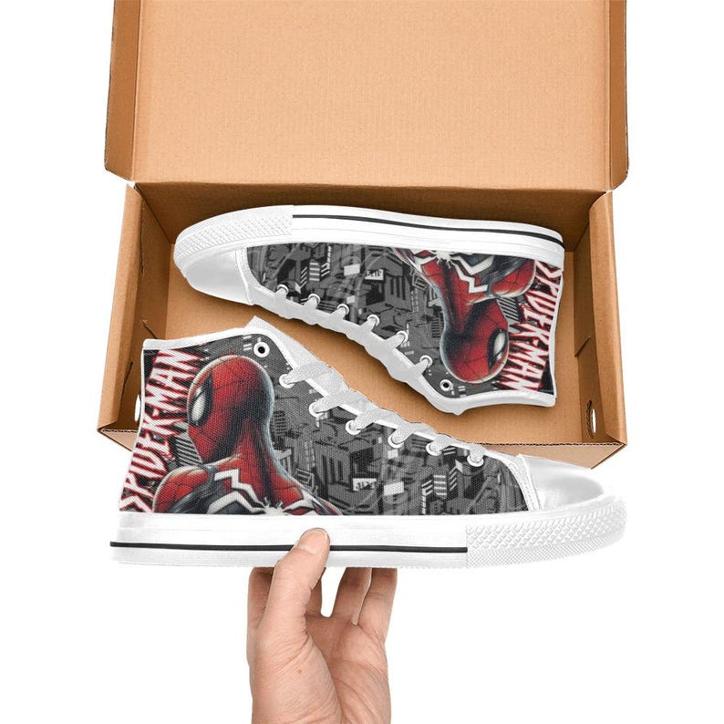 May include: High-top canvas sneakers featuring a Spider-Man design. The shoes have a white rubber sole and laces, with a black and gray cityscape background. The Spider-Man graphic is red and black, with the word "SPIDER-MAN" printed on the side.