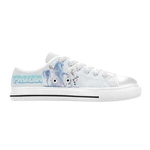 Peut inclure: Une basket basse en toile blanche avec un imprim&eacute; repr&eacute;sentant Elsa et Olaf de Frozen. La chaussure comprend un bout en caoutchouc blanc, des lacets blancs, des &oelig;illets m&eacute;talliques argent&eacute;s et une semelle blanche &eacute;paisse avec une fine ligne noire.