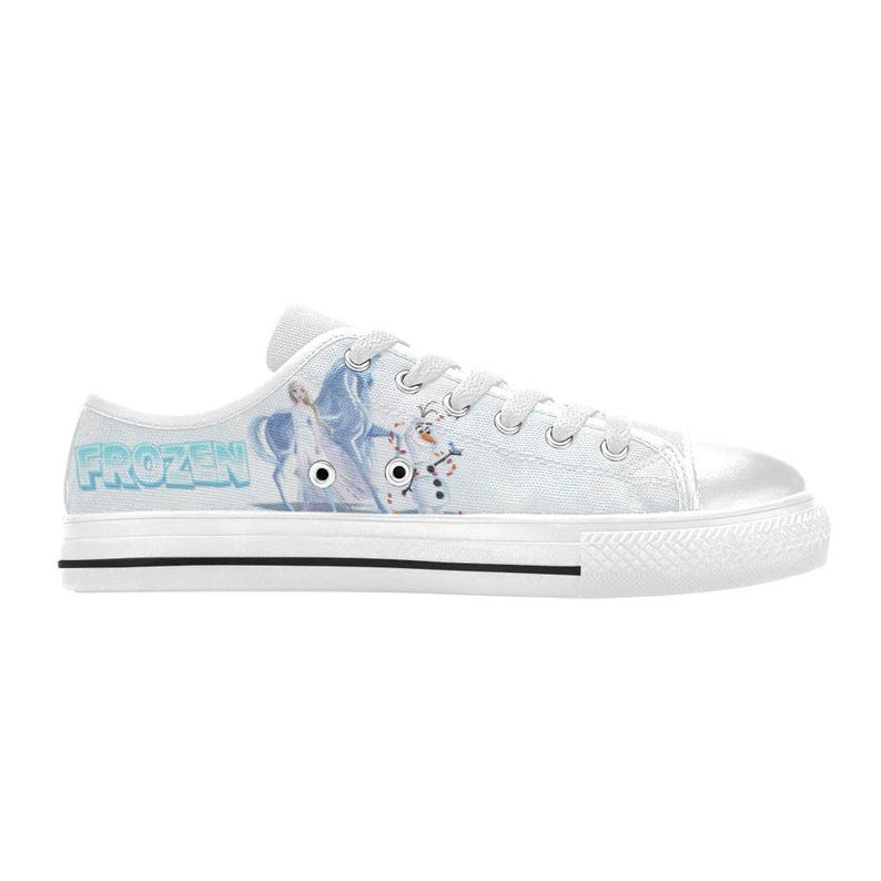 Peut inclure: Une basket basse en toile blanche avec un imprim&eacute; repr&eacute;sentant Elsa et Olaf de Frozen. La chaussure comprend un bout en caoutchouc blanc, des lacets blancs, des &oelig;illets m&eacute;talliques argent&eacute;s et une semelle blanche &eacute;paisse avec une fine ligne noire.