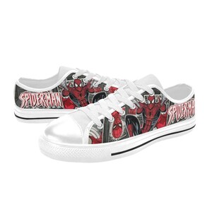May include: A pair of low-top canvas sneakers featuring a red and black comic book print of Spider-Man. The shoes have white laces, white rubber toe caps, and white soles. The text SPIDER-MAN is printed in a bold, stylized red font on the sides.