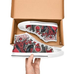 May include: A pair of high-top canvas sneakers featuring a red and black comic book print of Spider-Man. The shoes have white laces, white rubber toe caps, and white soles. The word Spider-Man is printed in red on the side of the canvas fabric.