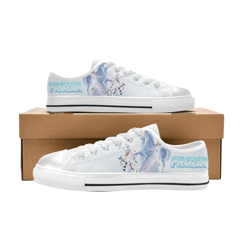 Peut inclure: Baskets basses en toile blanche avec un motif imprim&eacute; du personnage Olaf et le mot Frozen en lettres bleu clair. Les chaussures ont des lacets blancs, des &oelig;illets en m&eacute;tal argent&eacute;, un bout en caoutchouc blanc et une bande noire sur la semelle.