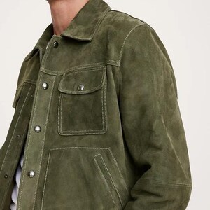 Puede incluir: Chaqueta de ante verde oliva con dos bolsillos en el pecho y dos bolsillos inferiores. La chaqueta tiene cuello y cierres de bot&oacute;n. Las costuras blancas acent&uacute;an las costuras y los bolsillos. Una prenda de vestir exterior elegante.