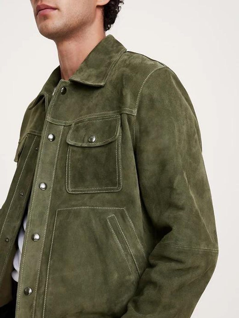 Puede incluir: Chaqueta de ante verde oliva con dos bolsillos en el pecho y dos bolsillos inferiores. La chaqueta tiene cuello y cierres de bot&oacute;n. Las costuras blancas acent&uacute;an las costuras y los bolsillos. Una prenda de vestir exterior elegante.