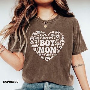 May include: A brown t-shirt with a white heart-shaped graphic that says "BOY MOM." The heart is filled with various illustrations, including cars, sports equipment, and game controllers. The word "EXPRESSO" is printed at the bottom.