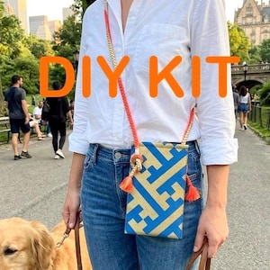 May include: A blue and gold patterned phone bag with a braided orange strap and tassel. The bag is worn crossbody style. The text "DIY KIT" is displayed in orange. The image is styled with a person wearing a white shirt and blue jeans.
