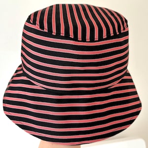 May include: A black and red striped bucket hat. The hat features horizontal stripes in black and red. The hat has a rounded crown and a downward-sloping brim. The hat is made of a fabric with a slight sheen.