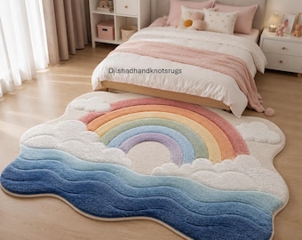Könnte beinhalten: Ein flauschiger Teppich mit Regenbogen- und Wolkenmotiv sowie dem Text Dilshadhandknotsrugs. Der Teppich zeigt einen mehrfarbigen Regenbogen über weißen Wolken und blauen Wellen, gefertigt mit einem strukturierten Flor in Blau-, Gelb- und Rosatönen.