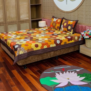 Pode incluir: Uma cama com um edredom colorido e duas almofadas a condizer. O edredom apresenta um padrão floral em tons de amarelo, laranja e castanho. Um tapete redondo com um desenho de flor de lótus está no chão. O quarto tem chão de madeira e um esquema de cores neutras.