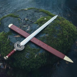May include: A decorative sword with a silver blade and a red and gold handle. The sword rests on a red sheath with gold accents. The sword's hilt features an ornate, circular design.
