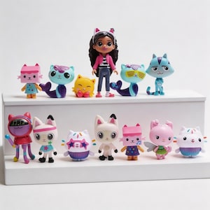 May include: A collection of colorful Gabby's Dollhouse figurines, including cat-themed characters and a doll. The figures are arranged on a white shelf against a white background. The characters have various designs and colors.
