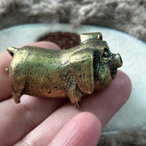 Peut inclure: Petite figurine de cochon en laiton détaillé. Le cochon est en position debout, les oreilles dressées. La figurine a une surface texturée et un aspect légèrement vieilli, suggérant qu'elle est vintage ou antique.