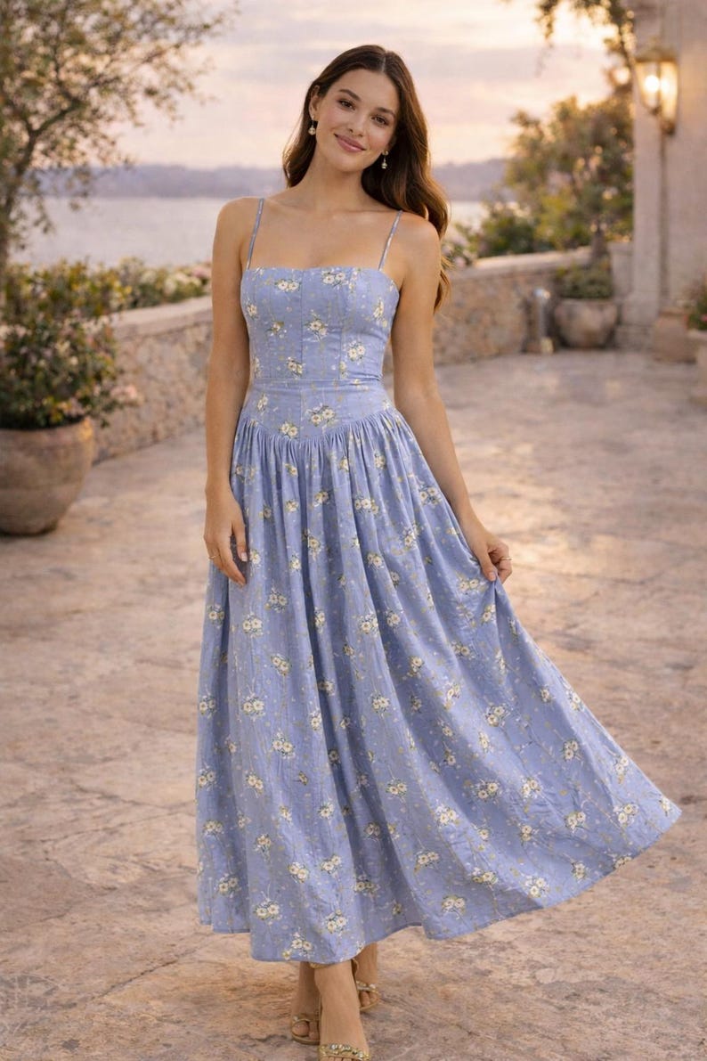 May include: A periwinkle blue midi dress featuring a square neckline, thin spaghetti straps, and a fitted bodice. The fabric is adorned with a small white and yellow floral pattern, and the skirt has a gathered waistline that flows into a full silhouette.