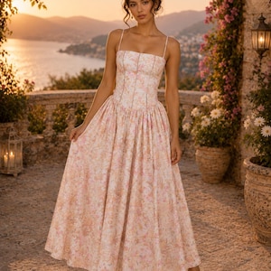 May include: A floor-length dress featuring a fitted bodice with thin spaghetti straps and a full, pleated skirt. The garment is made of a light-colored fabric adorned with a soft, muted floral pattern in shades of pink, peach, and cream.