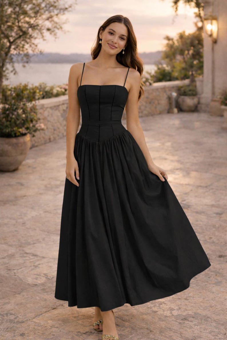 May include: A black midi dress featuring a fitted bodice with vertical seam detailing, a straight neckline, and thin spaghetti straps. The skirt is gathered at the waist, creating a full, flowing silhouette that falls below the knees.