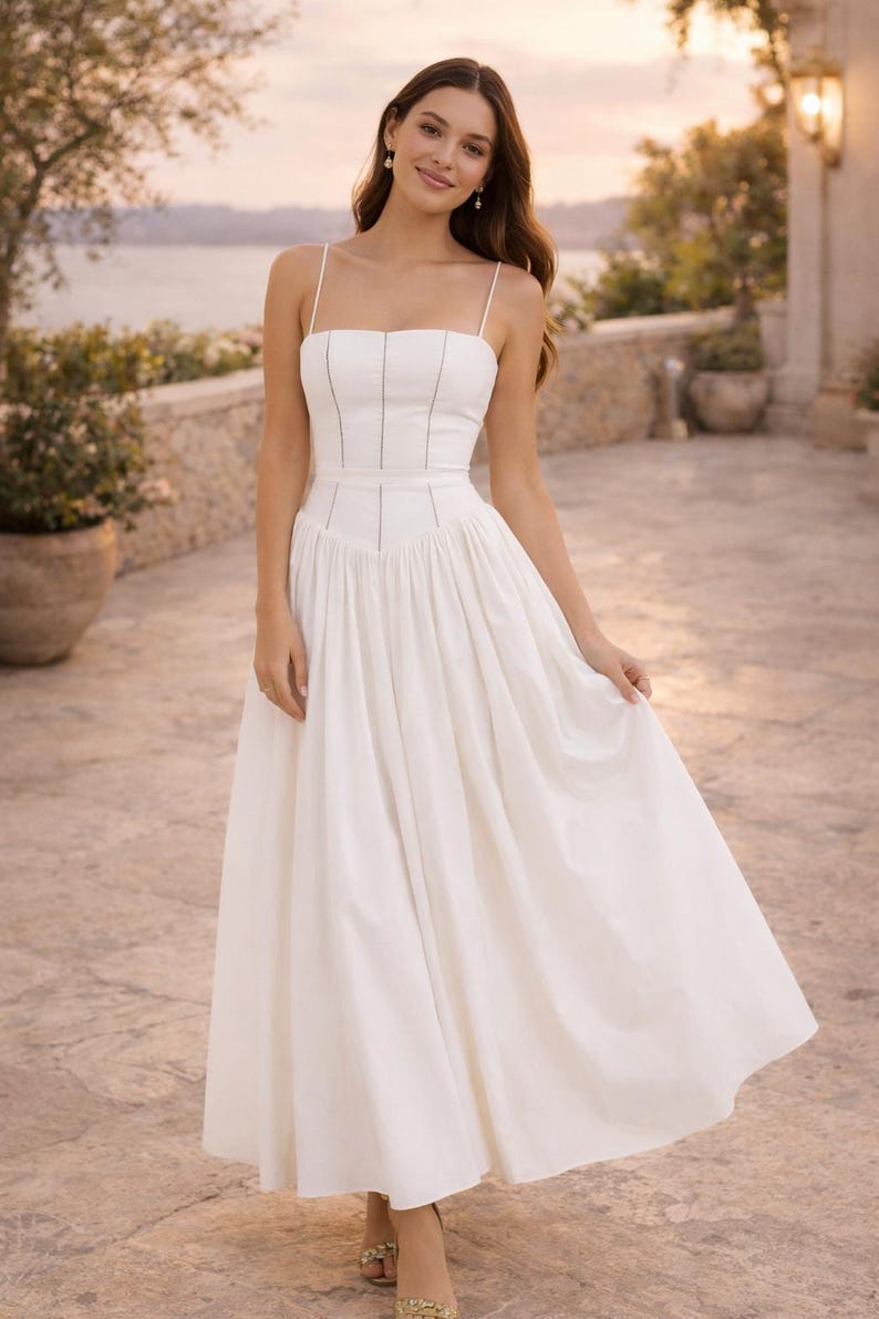 May include: A white midi dress featuring a fitted bodice with thin spaghetti straps and vertical seam detailing. The waistline is defined by a structured band, transitioning into a full, pleated skirt that falls to a mid-calf length.