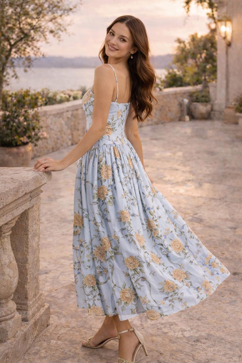 May include: A light blue midi dress featuring a floral pattern with yellow and orange blossoms and green leaves. The dress has thin spaghetti straps, a fitted bodice, and a full, pleated skirt that falls below the knees, paired with strappy heels.