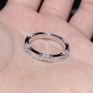 May include: A silver ring with a band of small, clear gemstones. The ring is marked with "G14K". The gemstones are set in a repeating pattern around the band. The ring is shown on a person's hand.